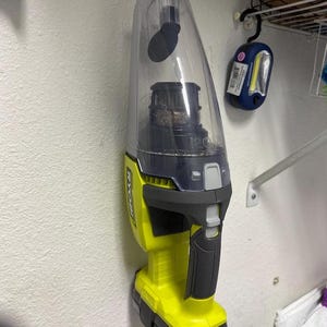 May include: A yellow and black handheld vacuum cleaner with a clear dustbin. The vacuum is mounted on a wall and has a Ryobi logo on the side.