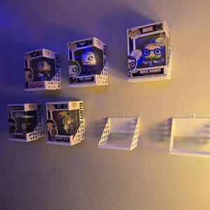 May include: Five Funko Pop vinyl figures in their original display boxes, including Caitlin Clark, The Joker, Bruce Banner, Walter Payton, and Elliott & E.T., arranged on white wall-mounted shelves, with two additional empty white shelves.