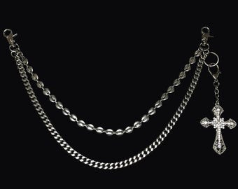 May include: Silver-toned chain accessory with two parallel chains and a decorative cross pendant. The chains have different textures, one with a curb link design and the other with oval beads. The cross is embellished with small, sparkling details.