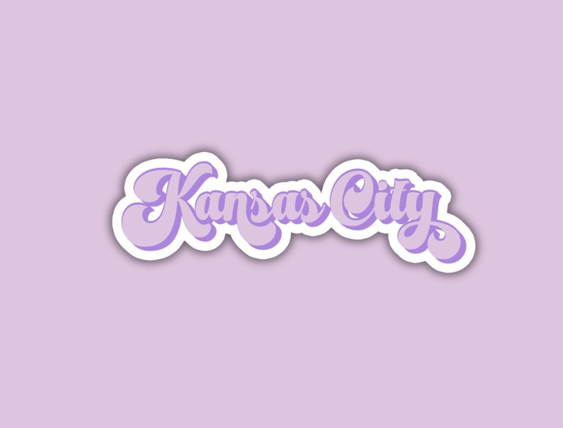 K&ouml;nnte beinhalten: Ein lilafarbener Aufkleber mit dem Text "Kansas City" in einer retro-kursiven Schrift.