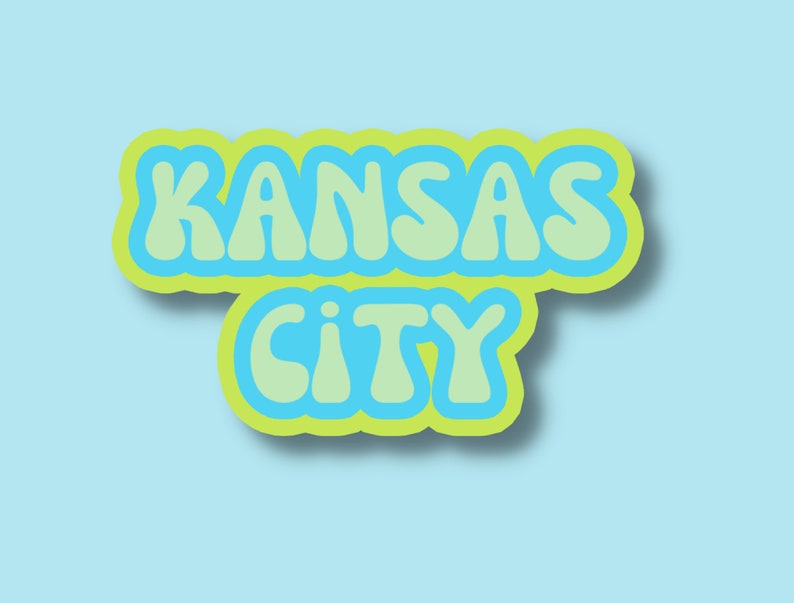 May include: A graphic design with the text "KANSAS CITY" in a retro, bubble-letter style. The letters are outlined in yellow and filled with light blue.