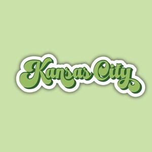 K&ouml;nnte beinhalten: Ein gr&uuml;ner und wei&szlig;er Aufkleber mit dem Text "Kansas City" in einer Retro-Schrift.
