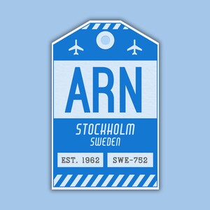 May include: Blue luggage tag with white text that reads "ARN STOCKHOLM SWEDEN EST. 1962 SWE-752". The tag has two small airplane icons and a circle in the top center.