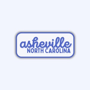 May include: A rectangular sticker with rounded corners, featuring the text "asheville NORTH CAROLINA" in a blue script font. The text is set against a white background with a blue border.
