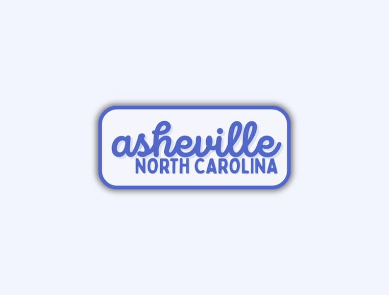 May include: A rectangular sticker with rounded corners, featuring the text "asheville NORTH CAROLINA" in a blue script font. The text is set against a white background with a blue border.