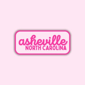 May include: A pink sticker with the text "asheville NORTH CAROLINA" in a rounded rectangle. The word "asheville" is in a cursive font, and "NORTH CAROLINA" is in a sans-serif font.