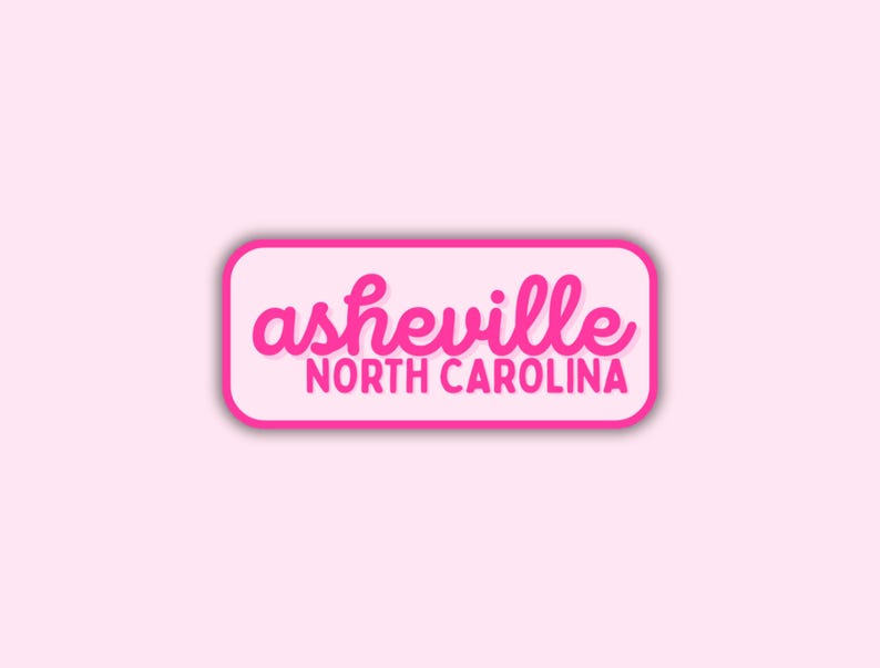 May include: A pink sticker with the text "asheville NORTH CAROLINA" in a rounded rectangle. The word "asheville" is in a cursive font, and "NORTH CAROLINA" is in a sans-serif font.