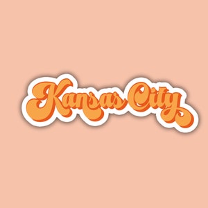K&ouml;nnte beinhalten: Ein Aufkleber im Retro-Stil mit dem Text "Kansas City" in orangefarbener Schrift mit wei&szlig;em Umriss.