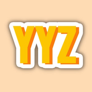 May include: A sticker with the letters "YYZ" in a bold, yellow font with an orange shadow and a white border. The sticker is set against a light peach background.