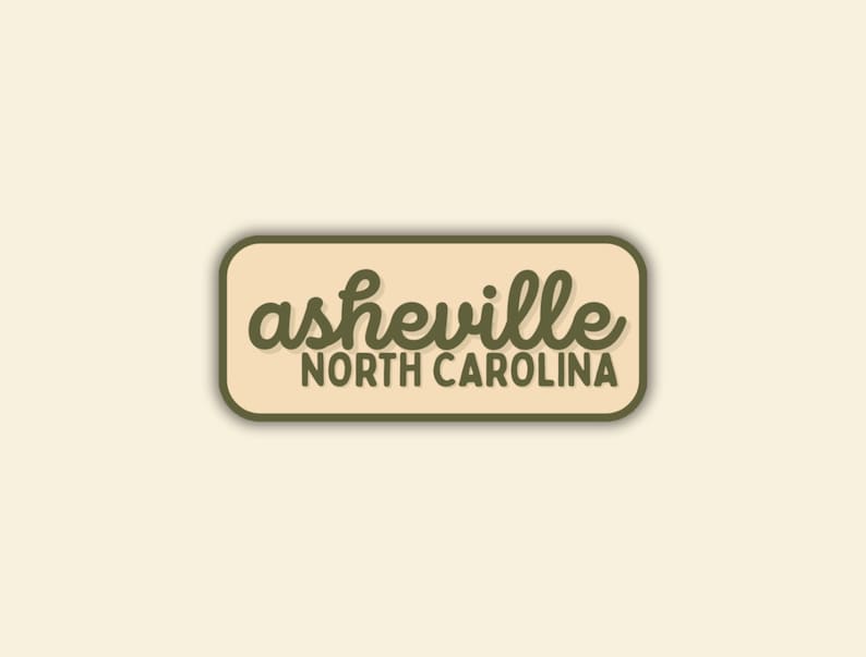 May include: A rectangular sticker with rounded corners. The sticker has a light tan background with a dark green border. The words "asheville" are in a cursive font, and "NORTH CAROLINA" is in a sans-serif font.