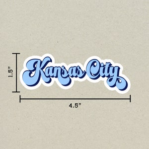 K&ouml;nnte beinhalten: Ein blauer und wei&szlig;er Aufkleber mit dem Text "Kansas City" in einem Retro-Schriftart-Stil. Der Aufkleber ist 4,5 Zoll breit und 1,5 Zoll hoch.