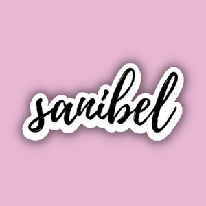 May include: A white sticker with a black handwritten word "sanibel" on a pink background.