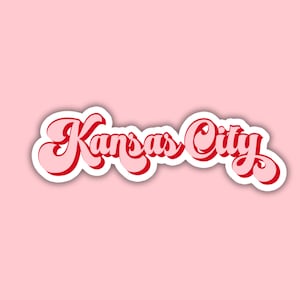 K&ouml;nnte beinhalten: Ein Retro-Grafikdesign mit dem Text "Kansas City" in Rot mit wei&szlig;em Umriss auf rosa Hintergrund.