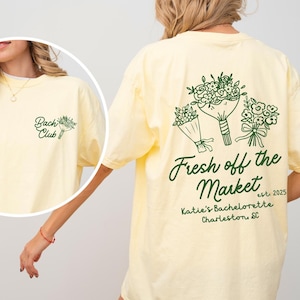 Może przedstawiać: Ż&oacute;łta koszulka z zielonym nadrukiem kwiat&oacute;w i tekstem "Fresh off the Market est. 2025 Katie's Bachelorette Charleston, SC".