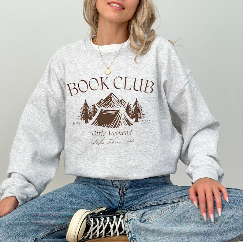 a woman sitting on the floor wearing a book club sweatshirt