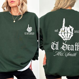 A woman wearing a green sweatshirt with white text and graphics on the back.