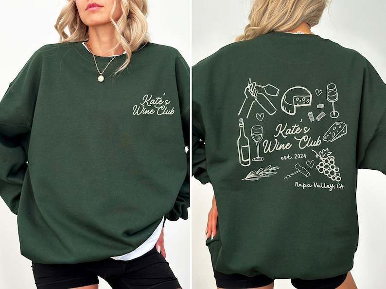 May include: A dark green crewneck sweatshirt with a design featuring the text 'Kate's Wine Club est. 2024 Napa Valley, CA' and wine-related illustrations.  The front shows a small 'Kate's Wine Club' text, while the back displays a more detailed design with wine bottles, glasses, grapes, and a cheese wedge. The sweatshirt is shown on a model from the front and back.