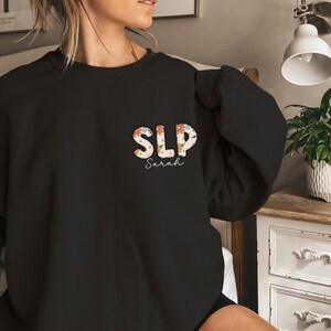 a woman sitting on a bed wearing a black sweatshirt