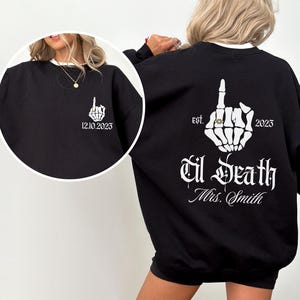 A woman wearing a black sweatshirt with white text and graphics on the back.