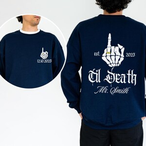A man wearing a navy blue sweatshirt with white text and graphics on the back.