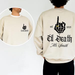 A man wearing a beige sweater with a graphic design on the back.