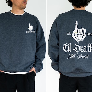 A man wearing a grey sweatshirt with white text and graphics on the back.
