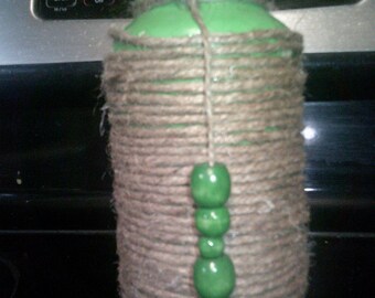 May include: A green glass jar wrapped in brown twine with a string of green beads hanging down the front.