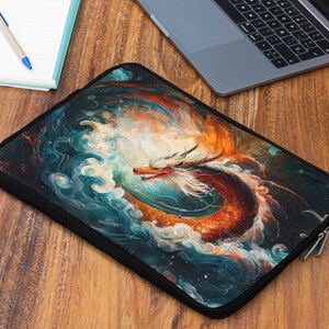 May include: Black laptop sleeve featuring a vibrant dragon design in shades of orange, red, and blue. The dragon is depicted amidst swirling clouds and waves. The sleeve is on a wooden surface, next to a notebook, pen, laptop, and a glass of beverage.
