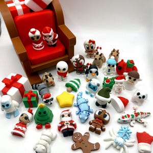 May include: A collection of Christmas-themed miniature figurines, including Santa Claus, snowmen, gingerbread men, and reindeer. A red sleigh with gifts is in the background. The figurines are in various colors, including red, white, green, and brown.