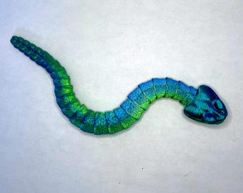 May include: A green and blue plastic snake toy with a segmented body and a detailed head.