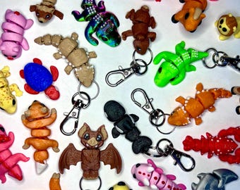 Puede incluir: Una colección de llaveros coloridos, pequeños y con forma de animales. Los llaveros están hechos de una variedad de materiales, incluyendo plástico, metal y tela. Presentan una variedad de animales, incluyendo un perezoso, un murciélago, un lagarto, un cangrejo, una abeja, una langosta, un pez y un dragón.