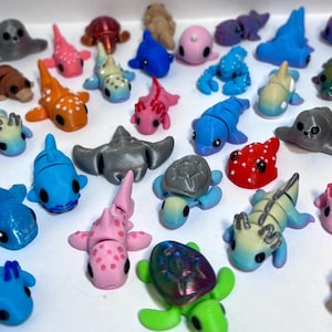 Op de afbeelding: Een verzameling kleurrijke, kleine, 3D-geprinte zeedieren, waaronder een haai, een schildpad, een zeester, een krab, een dolfijn, een zeepaardje, een kwal, een walvis, een zeehond en een rog.