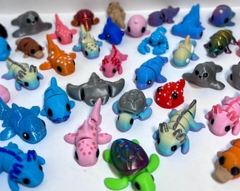 May include: A collection of colorful, small, 3D printed sea creatures, including a shark, a turtle, a starfish, a crab, a dolphin, a seahorse, a jellyfish, a whale, a seal, and a stingray.