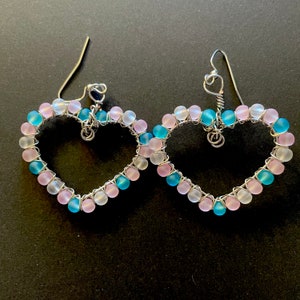 May include: A pair of heart-shaped earrings made with silver wire and pink and blue glass beads.