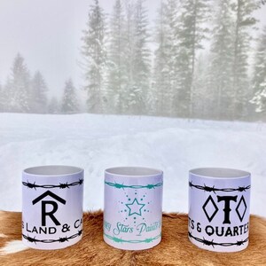 Puede incluir: Tres tazas de cer&aacute;mica blanca con dise&ntilde;os en negro y turquesa. Las tazas presentan dise&ntilde;os de alambre de p&uacute;as y texto que dice "R Land & Cattle", "Every Stars Paints a Story" y "T S & Quarter".