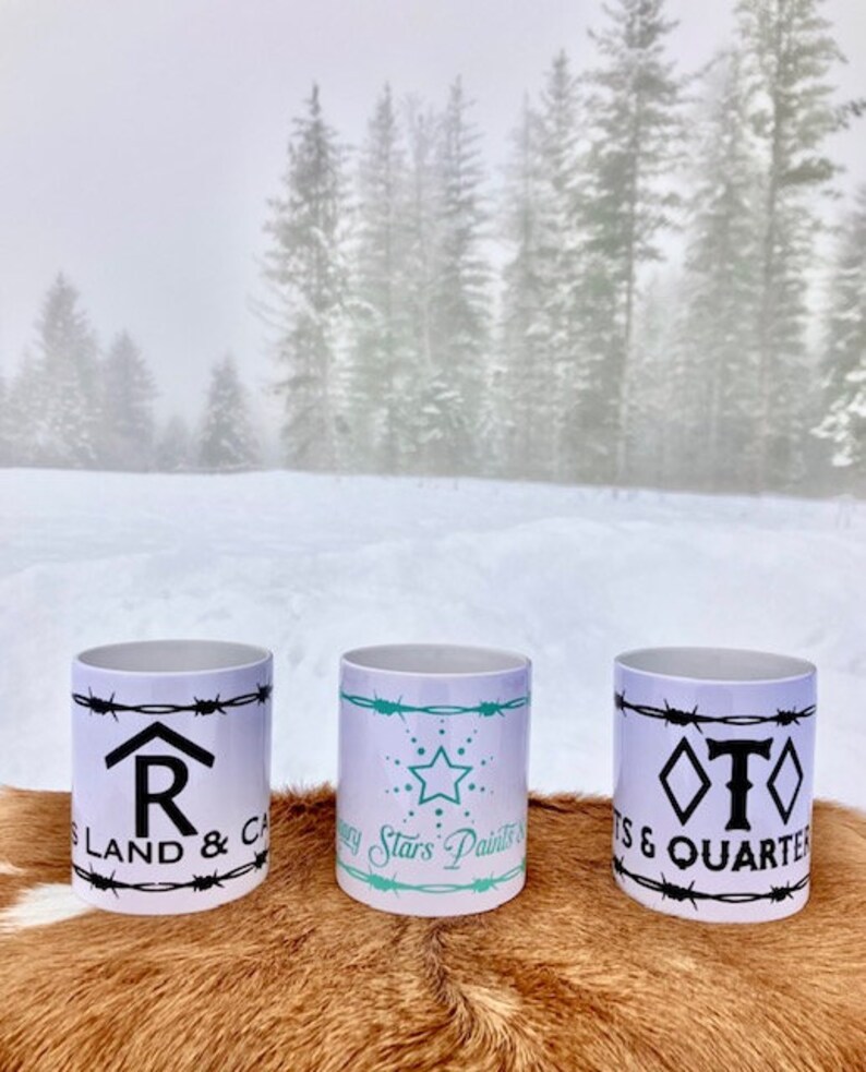 Puede incluir: Tres tazas de cer&aacute;mica blanca con dise&ntilde;os en negro y turquesa. Las tazas presentan dise&ntilde;os de alambre de p&uacute;as y texto que dice "R Land & Cattle", "Every Stars Paints a Story" y "T S & Quarter".