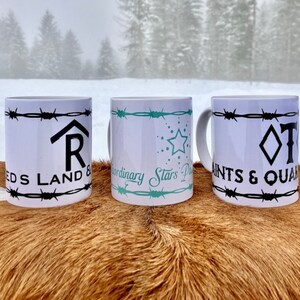 Puede incluir: Tres tazas de cer&aacute;mica blanca con dise&ntilde;os de alambre de p&uacute;as negro y texto diferente. La taza de la izquierda dice "REDS LAND &" con una "R" estilizada en forma de casa. La taza del medio dice "Extraordinary Stars" con un dise&ntilde;o de estrella turquesa. La taza de la derecha dice "SAINTS & QUAN" con una forma de diamante y una "T" estilizada.