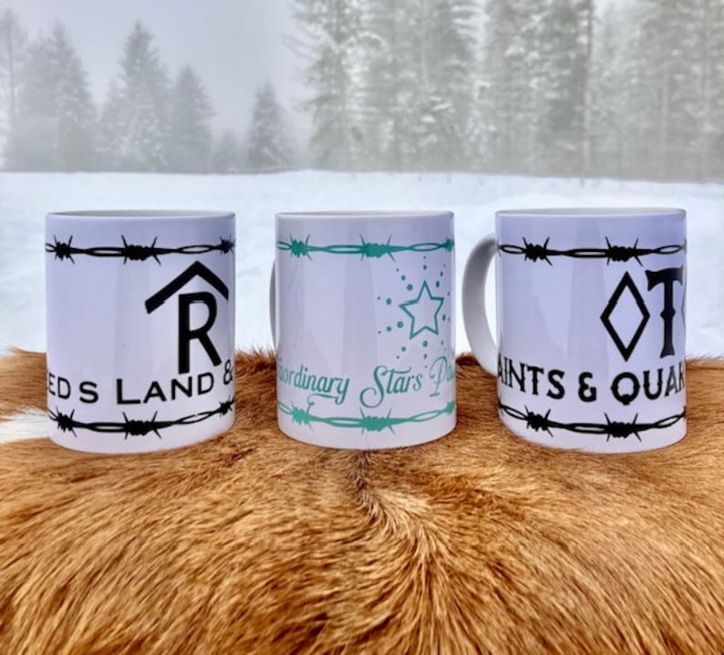 Puede incluir: Tres tazas de cer&aacute;mica blanca con dise&ntilde;os de alambre de p&uacute;as negro y texto diferente. La taza de la izquierda dice "REDS LAND &" con una "R" estilizada en forma de casa. La taza del medio dice "Extraordinary Stars" con un dise&ntilde;o de estrella turquesa. La taza de la derecha dice "SAINTS & QUAN" con una forma de diamante y una "T" estilizada.