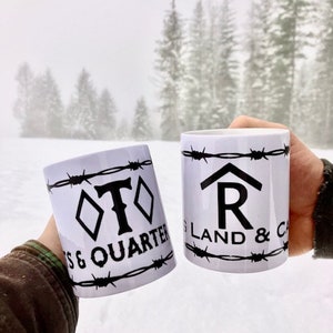 Puede incluir: Dos tazas de cer&aacute;mica blanca con dise&ntilde;os de alambre de p&uacute;as negros. Una taza dice "T & Quarter" y la otra dice "R Land & Cattle".