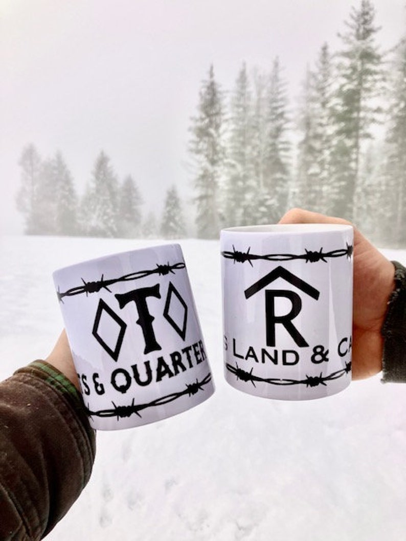 Puede incluir: Dos tazas de cer&aacute;mica blanca con dise&ntilde;os de alambre de p&uacute;as negros. Una taza dice "T & Quarter" y la otra dice "R Land & Cattle".