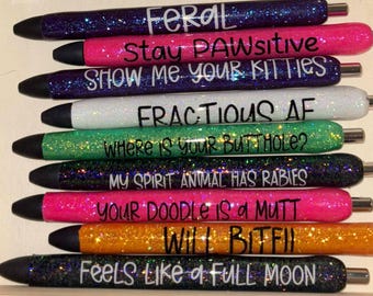 Puede incluir: Una colección de nueve bolígrafos con purpurina en varios colores, incluyendo morado, rosa, blanco, verde, negro y naranja. Cada bolígrafo presenta texto en negro o blanco con frases como FERAL, Stay PAWSITIVE, SHOW ME YOUR KITTIES, FRACTIOUS AF, WHERE IS YOUR BUTTHOLE?, MY SPIRIT ANIMAL HAS RABIES, YOUR DOODLE IS A MUTT, Will BITFII y Feels like a full moon.