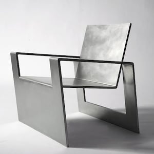 Può includere: Una sedia moderna e minimalista in metallo con finitura argentata. La sedia ha una struttura rettangolare e un'unica seduta ampia.