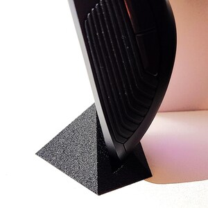 May include: A black computer mouse with a textured design and a purple light on the side. The mouse is sitting on a black triangular stand.