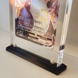 Może przedstawiać: Przezroczysta akrylowa gablota z czarną podstawą, prezentująca japońską kartę kolekcjonerską Pokemon z holograficznym obrazem postaci Pokemon. Tekst na karcie brzmi "VMAX-JP-10" i "ツメできりさく キョタイゴクエン".