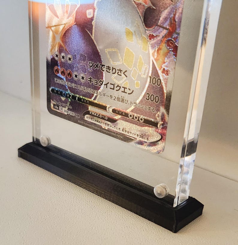 Może przedstawiać: Przezroczysta akrylowa gablota z czarną podstawą, prezentująca japońską kartę kolekcjonerską Pokemon z holograficznym obrazem postaci Pokemon. Tekst na karcie brzmi "VMAX-JP-10" i "ツメできりさく キョタイゴクエン".