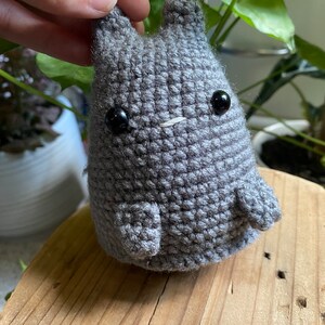 Puede incluir: Un animal de peluche gris tejido a crochet con grandes ojos negros. El animal tiene un cuerpo redondo y orejas pequeñas.