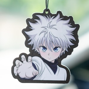 May include: A decorative air freshener featuring a cartoon character with white hair and blue eyes. The character is wearing a white outfit with a black collar and is reaching out with one hand. The air freshener has a black border and is hanging from a black string.