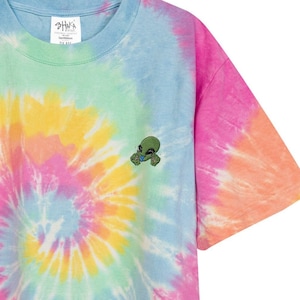 May include: A tie-dye t-shirt with a spiral pattern in shades of blue, green, yellow, orange, and pink. A small green alien graphic is embroidered on the right side of the shirt.
