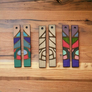 Peut inclure: Six ornements rectangulaires en bois avec différents motifs géométriques colorés. Les ornements sont peints dans des tons de bleu, vert, rouge, violet et marron.