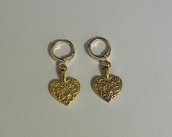 May include: A pair of gold filigree heart earrings with silver hoops. The hearts are detailed with intricate designs and hang from the hoops.